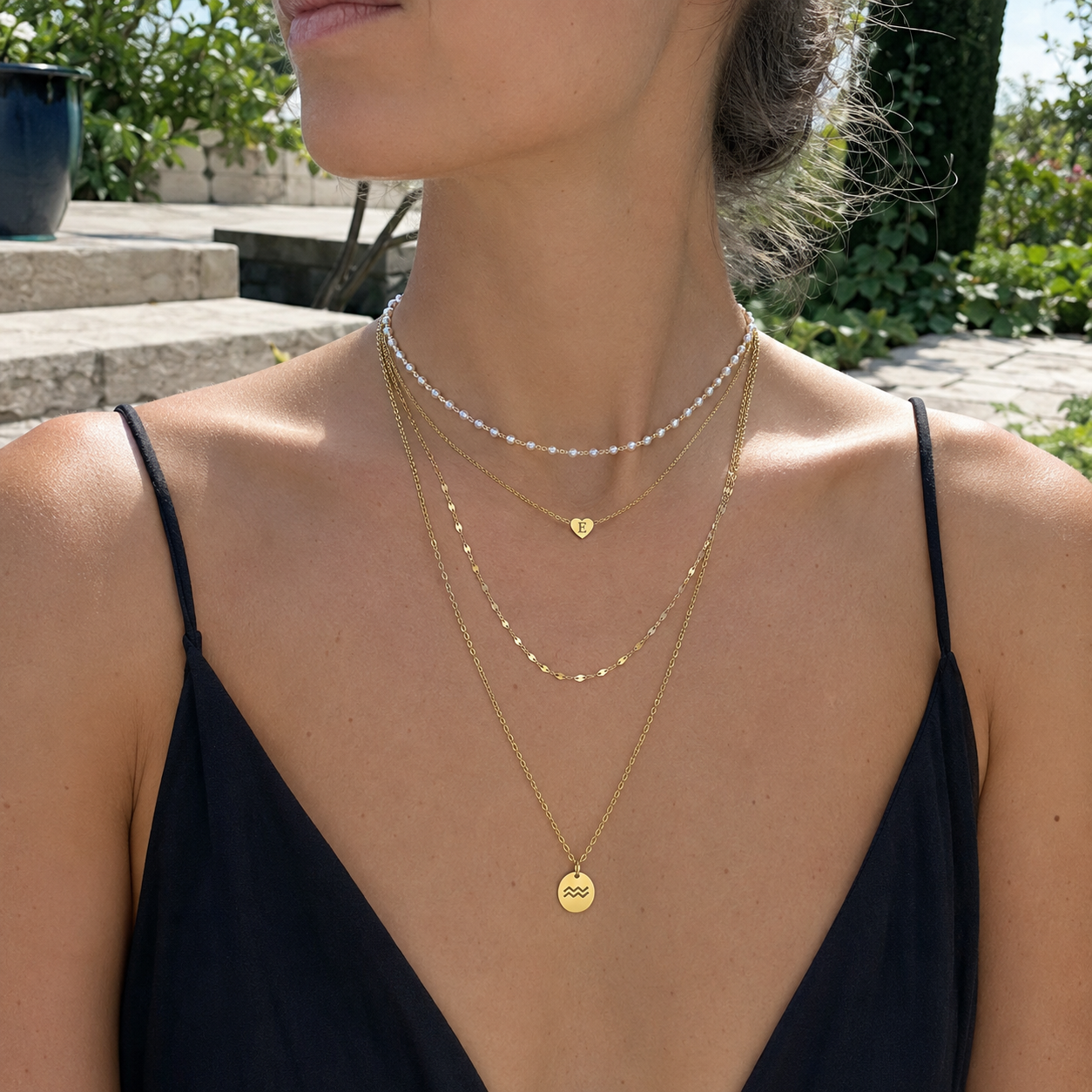 Gold-tone stainless steel maximalist layered necklace stack with pearl choker, heart initial pendant, and zodiac charm